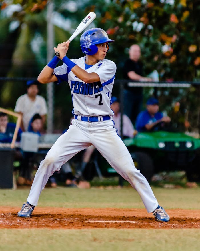 Teen baseball player in uniform ready to swing during a game on a grassy field.